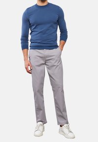 Blå stickad tröja med lång ärm, grå byxor med diskreta ränder och vita sneakers. Klädseln har en figursydd design och mjuk textur.