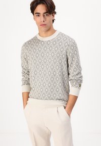 Light gray knit sweater featuring a diamond pattern, ribbed crew neck, and cuffs. Accented with a small yellow logo on the sleeve.
