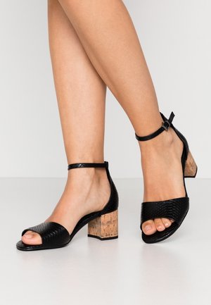 Sorte åbne sandaler med læderremme med tekstur og en blokhæl af kork. Har en ankelrem med spænde for en sikker pasform.