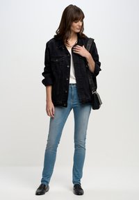 Melnas denima jaka ar pogu priekšpusi, pārāk liela izmēra, balts tops, gaiši zili šaurie džinsi un melni loafers. Aksesuāri ietver melnu somu.