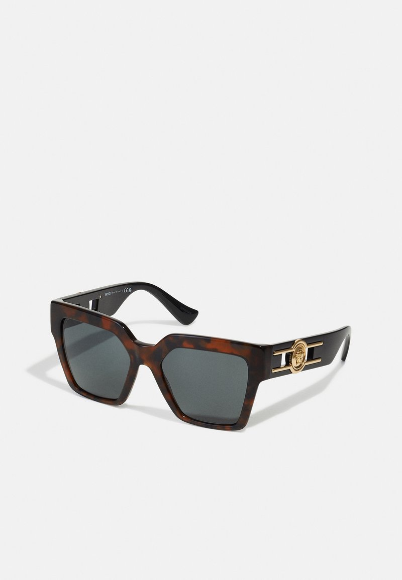 Sonnenbrille im Schildpatt-Design mit einem massiven, sechseckigen Rahmen. Dunkelgraue Gläser und goldenes Beschlagmaterial an den Bügeln mit einem Logo-Akzent.
