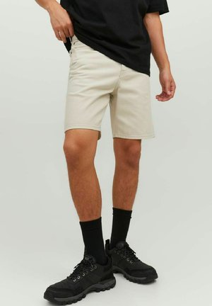 Pantaloni corti beige con taglio dritto e orlo, abbinati a una t-shirt nera, calzini neri e sneakers nere. Tessuto morbido, design casual.