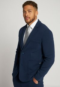 Giacca da abito blu navy realizzata in tessuto morbido, caratterizzata da un'unica chiusura a bottone, rever a punta e due tasche frontali con cuciture decorative.