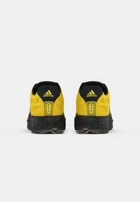 Μαύρα και κίτρινα αθλητικά παπούτσια με υφασμένο πλέγμα στο επάνω μέρος, μαξιλαράκι στη φτέρνα και έντονα κίτρινα στοιχεία κοντά στη σόλα και στο λογότυπο της μάρκας.