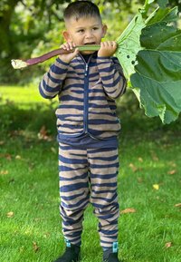 Randig fleece-loungewear-set i beige och marinblått, innehållande en jacka med dragkedja och matchande byxor. Barnet håller en stor bladgrönsak.