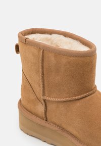 Boots chevilles en suède marron avec une doublure en crème douce, un dessus texturé, des coutures renforcées et une semelle en caoutchouc plate pour une bonne adhérence.