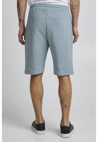 Shorts en coton bleu clair avec une taille élastique, coupe jusqu'aux genoux, poches latérales et texture lisse. Portés avec des baskets noires.