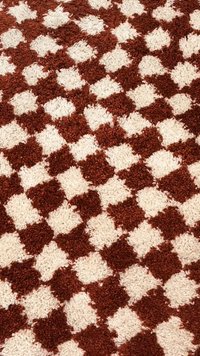 Barna és fehér geometriai mintájú szőnyeg, puha, texturált négyzetekkel váltakozó színekben, sakktáblaszerű mintát alkotva.