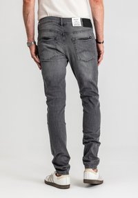 Szare jeansy z denimu o dopasowanym kroju, z tylnymi kieszeniami i czarną metką na pasku. Zaprezentowane z białymi trampkami.
