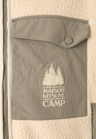 Beige fleecová bunda s šedou kapsou na cvoky, která má bílý grafický motiv stromů a text "Maison Kitsuné Camp."