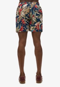 Szorty kąpielowe w wzory na granatowym tle, z dużymi, tropikalnymi kwiatami w kolorze czerwonym i kremowym. Wykonane z lekkiego materiału z elastycznym pasem.