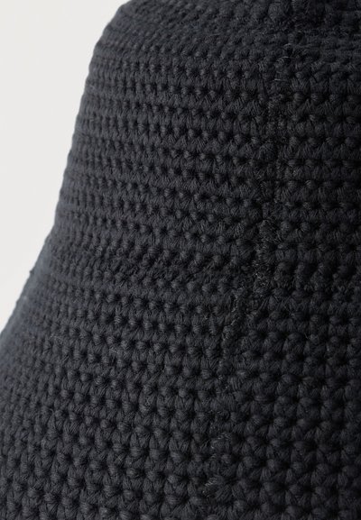 Κοντινή λήψη μαύρου πλεκτού υφάσματος με σφιχτούς, ομοιόμορφους βρόγχους και ορατή ραφή που διατρέχει κάθετα την υφή.