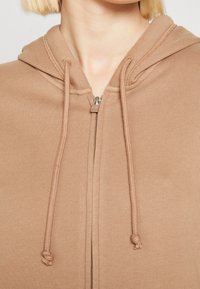 Brown zip-up hoodie with a adjustable drawstring hood, featuring a smooth texture and metallic zipper detail. Simple design without patterns.