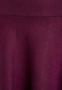 Zbliżenie na głęboki fioletowy dzianinowy materiał z prążkowaną teksturą u góry i gładkim splotem poniżej.