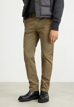 Khaki chinos with a slim fit, made from cotton. Features belt loops, side pockets, and a smooth texture. Worn with black rubber boots.