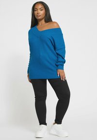 Sweter dziany z odkrytymi ramionami w jasnoniebieskim kolorze z teksturowanym wzorem, w zestawieniu z czarnymi legginsami i białymi sneakersami. Luźny krój i długie rękawy.