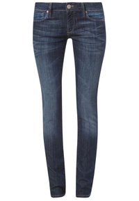 Jeans ajustados de tela de denim azul oscuro. Entre sus características se incluyen un clásico diseño de cinco bolsillos, remaches de cobre y un acabado ligeramente desgastado.