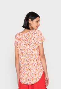 Camisola de mangas curtas com padrões florais em tons de laranja e rosa, apresentando uma bainha arredondada, padrão floral e um corte relaxado.