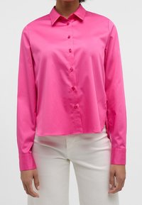 Bright pink long-sleeve button-up shirt with a collar, made of smooth fabric, featuring front buttons and a slightly curved hemline.