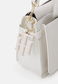 Borsa a mano bianca in pelle con finitura testurizzata, dotata di una chiusura in metallo dorato e un charm monogrammato rosa pallido.