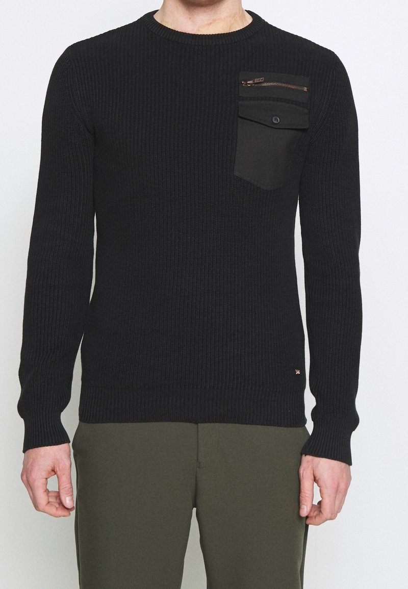 Schwarzer gerippter Pullover mit langen Ärmeln, Rundhalsausschnitt und einer Vordertasche mit Reißverschluss. Strukturiertes Gewebe mit figurbetonter Passform.