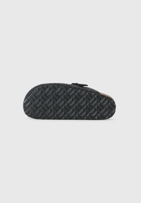 Black shoe sole with a textured rubber tread pattern, featuring a flat, rounded shape and a smooth upper edge.