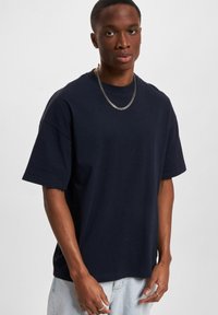 Mørkeblå bomulls T-skjorte med avslappet passform, korte ermer og rund hals. Brukes sammen med lyse jeans og en sølvkjede.