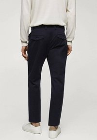 Pantalons navy en coton avec une coupe ajustée, dotés de deux poches arrière à bouton et portés avec des baskets blanches.