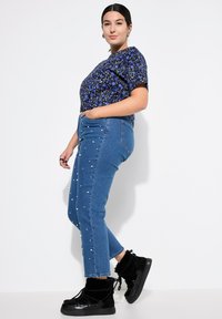 Top corto a maniche corte floreale blu abbinato a jeans azzurri chiari con decorazioni in perle bianche. Stivali alla caviglia in pelliccia sintetica nera completano il look.