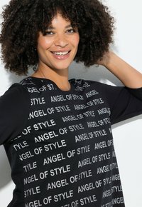 Schwarzes Oberteil mit dem Schriftzug "ANGEL OF STYLE" in Weiß, Rundhalsausschnitt und langen Ärmeln, hergestellt aus glänzendem Stoff mit einer lockeren Passform.