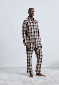 Herren-Pyjama-Set im Karomuster mit beige, marineblau und roten Farben. Hergestellt aus weichem Stoff, mit einem Langarmhemd mit Knöpfen und einer passenden Hose.