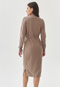 Robe tricotée longue marron avec un col côtelé, des manches longues, des fentes sur les côtés et une ceinture assortie, dotée d'un tissu doux et texturé.
