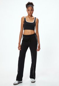 Zwarte crop top met witte bies en zwarte sweatpants met witte zijstrepen. Model draagt zwarte en witte sport-schoenen.