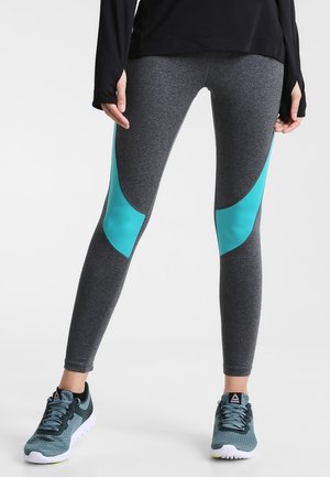 Leggings gris avec des panneaux en teal, fabriqués en tissu extensible, dotés d'une coupe ajustée et de couleurs contrastées, associés à des chaussures de sport.