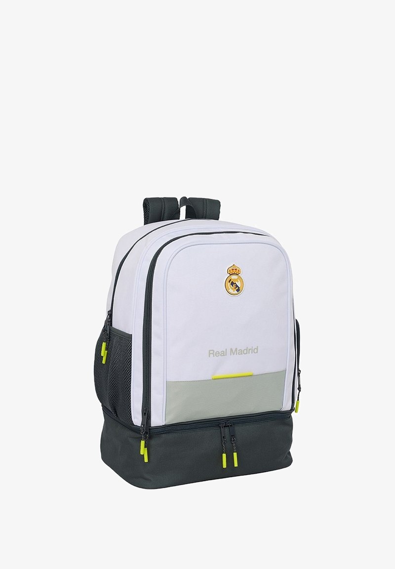 Zaino bianco e grigio scuro con scomparto principale con zip, tasche laterali in rete, dettagli gialli e logo del Real Madrid sul davanti.