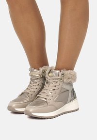 Zapatillas altas color topo con cuello de piel sintética, detalles metálicos, paneles laterales texturizados y una suela de goma blanca; diseño con cordones para un ajuste seguro.