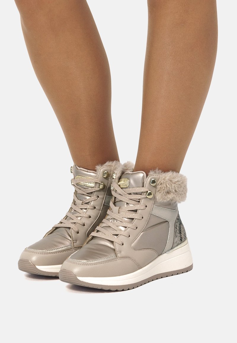 Zapatillas altas color topo con cuello de piel sintética, detalles metálicos, paneles laterales texturizados y una suela de goma blanca; diseño con cordones para un ajuste seguro.