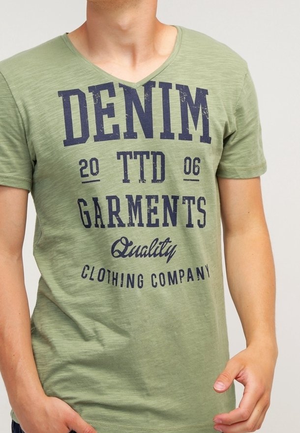 Zelené tričko s výstřihem do V vyrobené z měkké bavlny, s námořnickým potiskem textu: "DENIM TTD 2006 GARMENTS Quality CLOTHING COMPANY." Jednoduchý design.