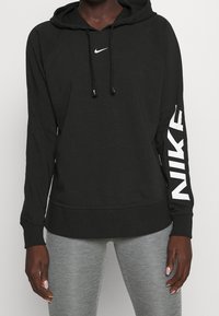 Czarna bluza z kapturem z przednią kieszenią kangurka, białym logo Nike na piersi i rękawie, kapturem ze sznurkiem oraz ściągaczami na rękawach.