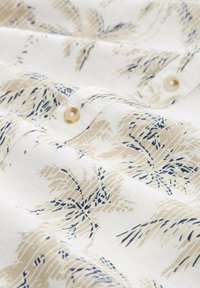 Tissu léger avec un fond crème orné d'un motif de feuilles de palmier beige et bleu. Comprend des boutons en matériau clair.