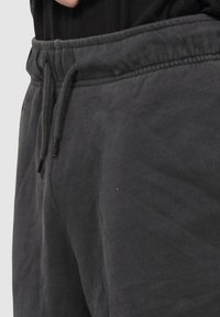 Nahaufnahme einer Person, die dunkelgraue Sweatpants mit elastischem Bund und Kordelzug trägt, kombiniert mit einem schwarzen Oberteil.