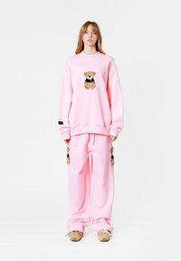 Sudadera rosa de gran tamaño y pantalones de chándal a juego con bordado de osito de peluche en la parte frontal y los laterales. Tela suave, corte holgado y cintura con cordón.
