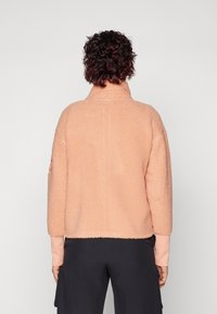 Pullover in pile testurizzato di colore rosa chiaro, con colletto alto, maniche a tre quarti e una vestibilità comoda, abbinato a pantaloni scuri.