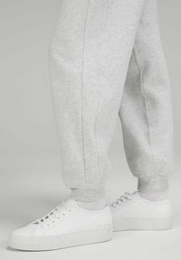 Weiße Leder-Sneaker mit glatter Textur, runder Zehenpartie und dicker Sohle, kombiniert mit grauen schmal zulaufenden Sweatpants mit elastischen Bündchen.