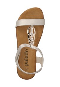 Sandalia plana beige con parte superior de cuero suave, tres correas superpuestas y un detalle metálico circular en la parte delantera. Plantilla con acabado similar al ante.