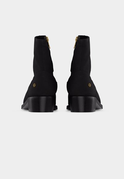 Black mid-calf boots with block heels, gold side zippers, and small gold circular logos on the outer heels, shown from the back.