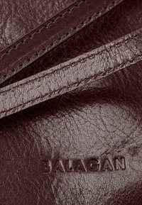 Superficie in cuoio testa di moro con texture, dotata di due cinturini cuciti e con il nome del marchio inciso "BALAGAN" visibile nell'angolo in basso a destra.