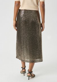 Gonna midi marrone con paillettes, dalla forma dritta. Presenta una texture liscia e un leggero scintillio, abbinata a tacchi neri con cinturini.
