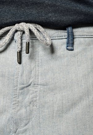 Jean en denim bleu clair avec un cordon de serrage tissé gris muni de pointes en métal et une taille contrastante en bleu foncé.
