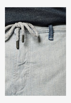 Jean en denim bleu clair avec un cordon de serrage tissé gris muni de pointes en métal et une taille contrastante en bleu foncé.